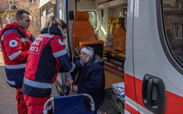 Two health workers tend to an injured elderly woman sitting in the doorway of an ambulance