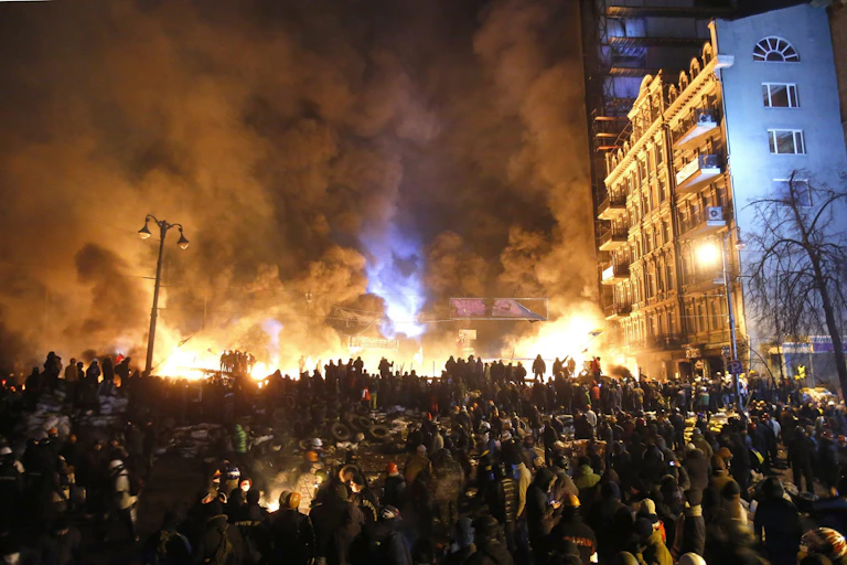 A large crowd of people stand in front of a fire and huge plumes of smoke