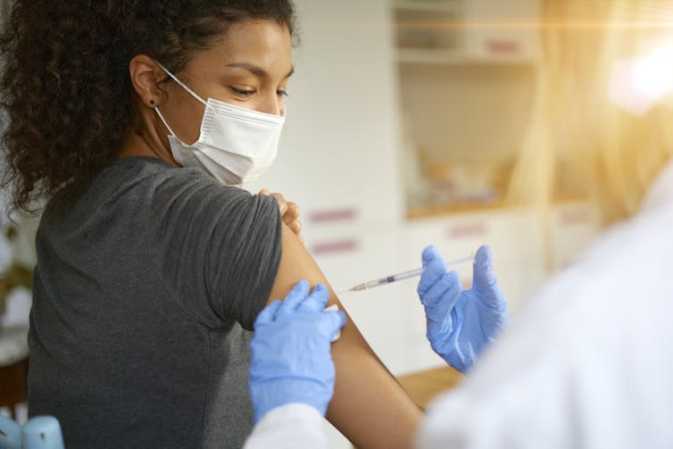 A young woman getting a vaccine shot on her upper arm.
