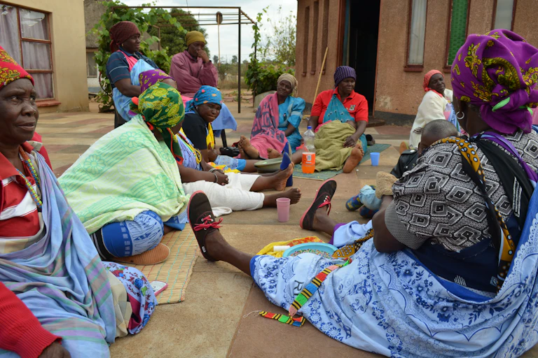 A group of people sit on the floor wearing colourful outfits.