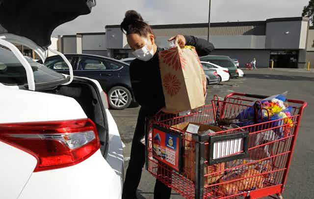 A woman loads groceries into the trunk of a car