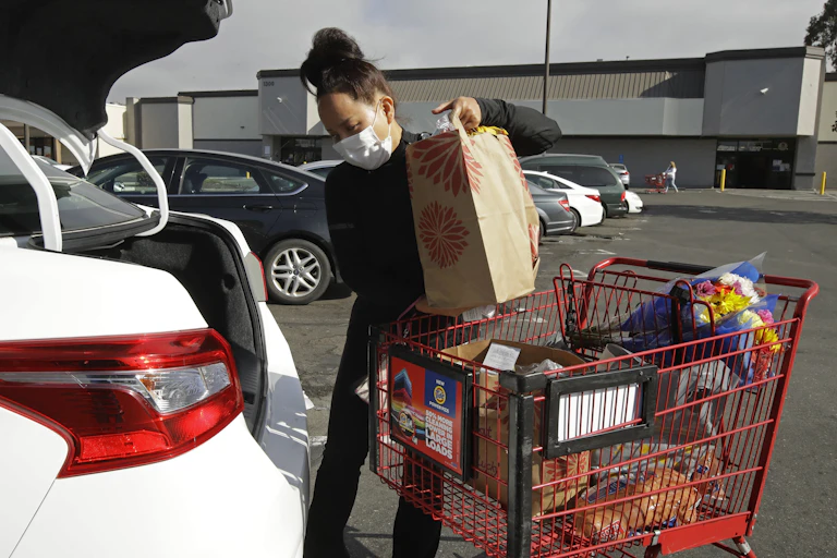 A woman loads groceries into the trunk of a car