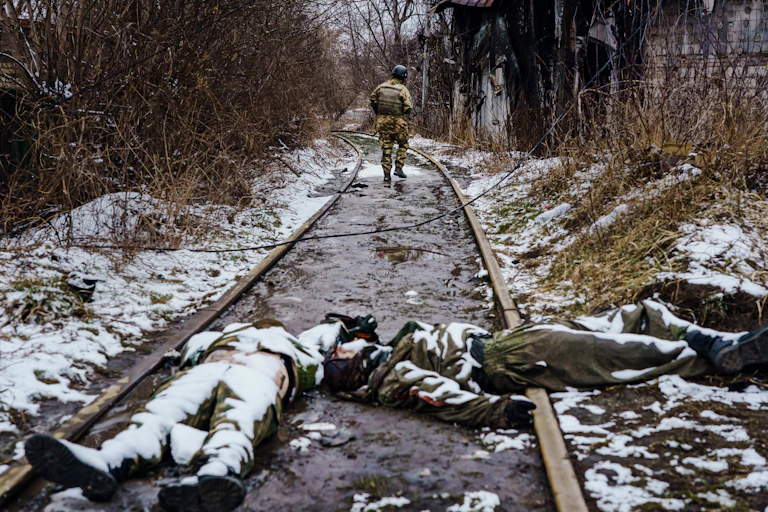 Two dead Russian soldiers, wearing uniforms and covered with snow, lie on railroad tracks as a Ukrainian soldier walks away from them along the track..