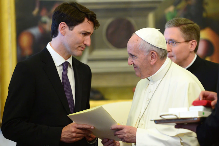A man in a black suit seen with a man in white clerical garments including a skullcap.