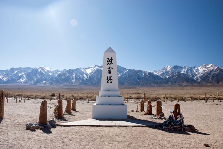 A white monument featuring an inscription in Japanese characters in a desert setting with snow-covered mountains in the background.