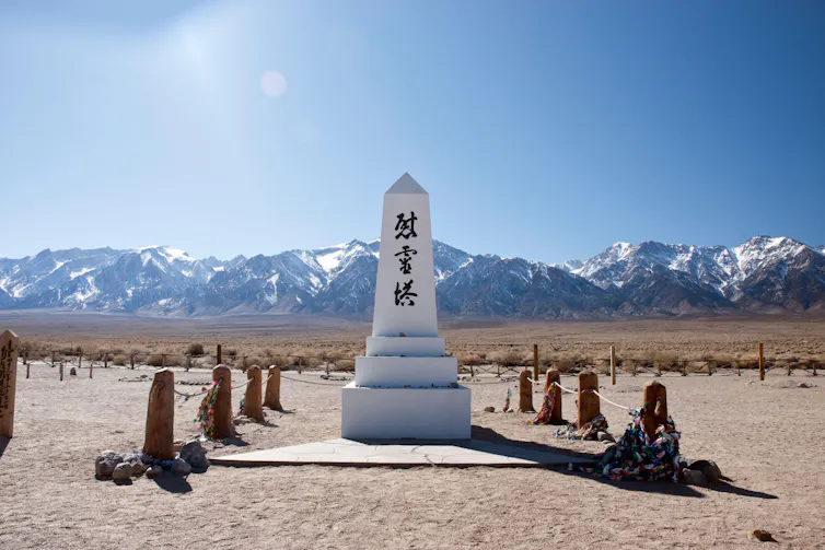 A white monument featuring an inscription in Japanese characters in a desert setting with snow-covered mountains in the background.