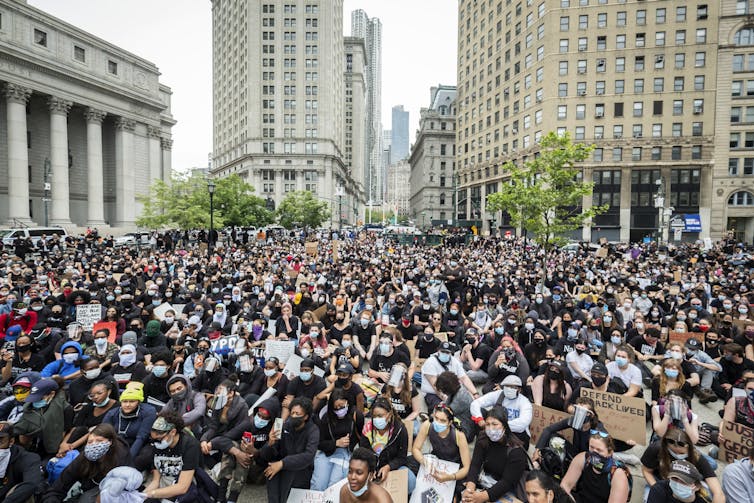 Thousands of protesters are sitting down in the middle of street.