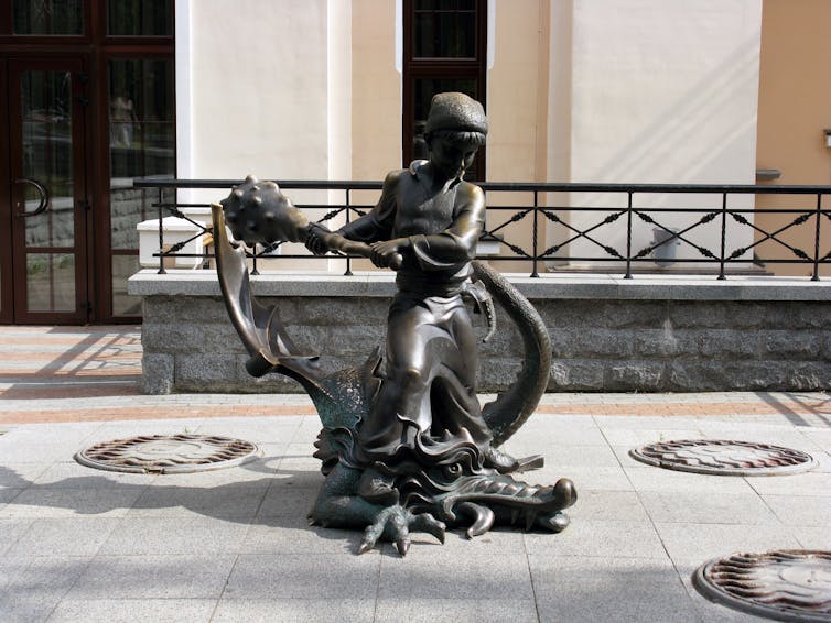 Estatua de bronce de una niña que mata a un gran dragón con un garrote