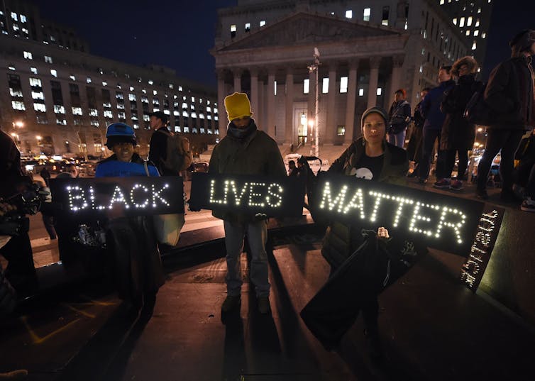 Tres personas sostienen carteles que dicen Black Lives Matter.