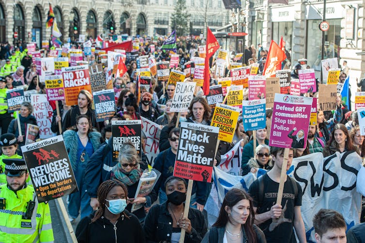 Thousands of people are marching in the street and carrying signs that demand an end to racism.