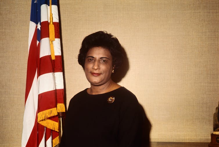 A woman stands in front of a U.S. flag