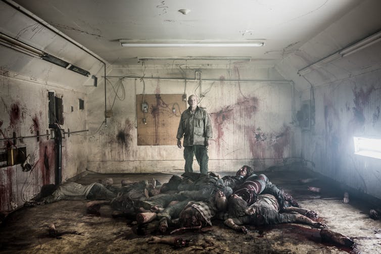 a man stands over a pile of zombies in a room with blood-stained walls