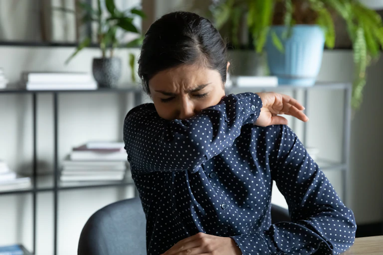 Woman coughs into her arm