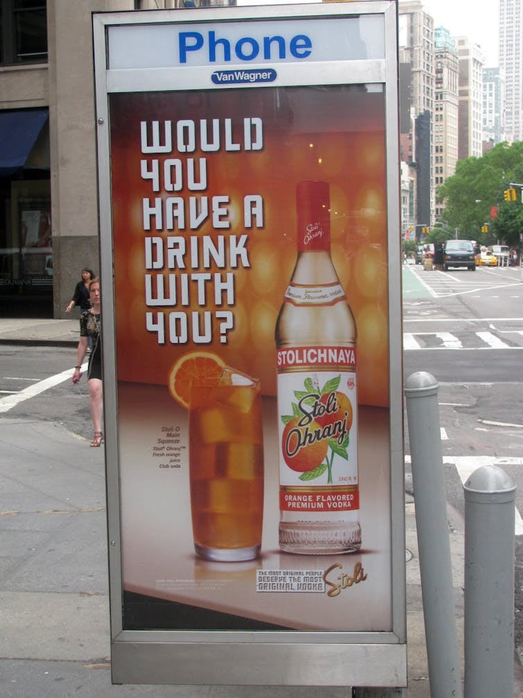 A poster advertising a bottle of vodka on the side of a phone booth.