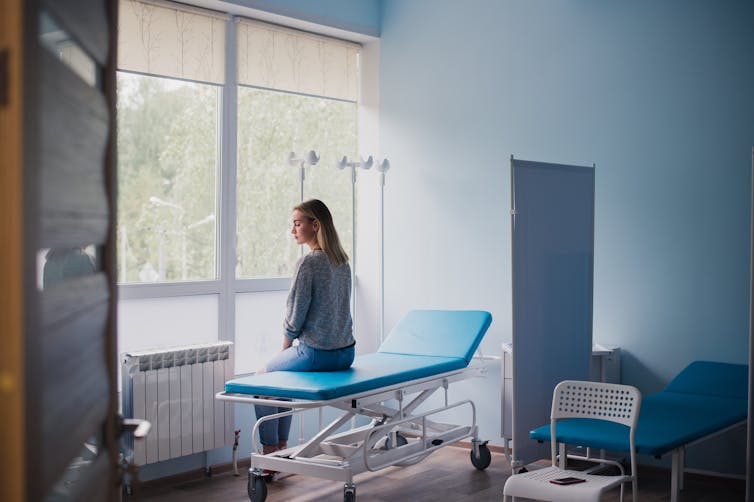 Young woman sitting on a hospital bed waits alone in an examination room.