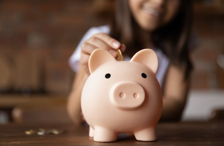 Child placing coin into a piggy bank.