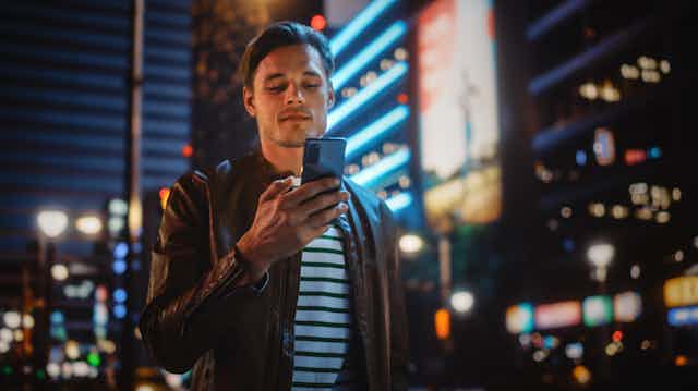 A young man looks at his phone. The background is a city at night.
