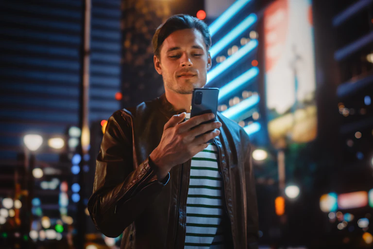 A young man looks at his phone. The background is a city at night.