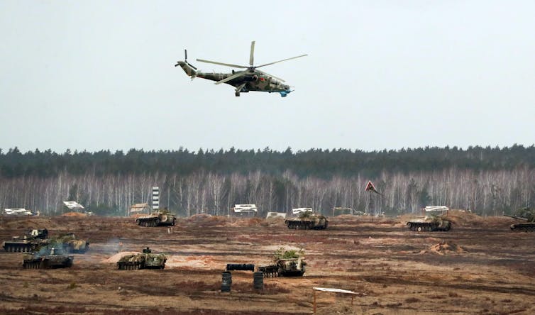 A helicopter flies above military vehicles in joint exercises between Russia and Belarus, February 2022.