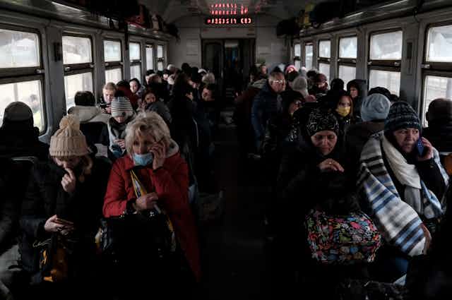 People fleeing Ukraine sitting on a train wrapped in blankets.
