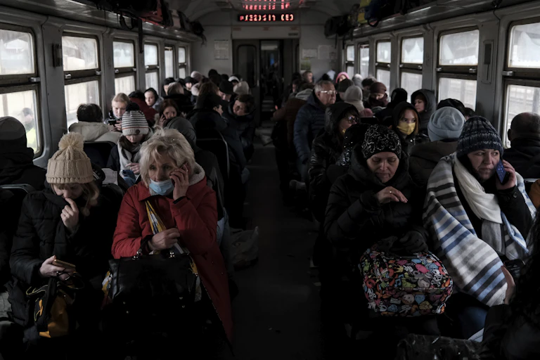 People fleeing Ukraine sitting on a train wrapped in blankets.
