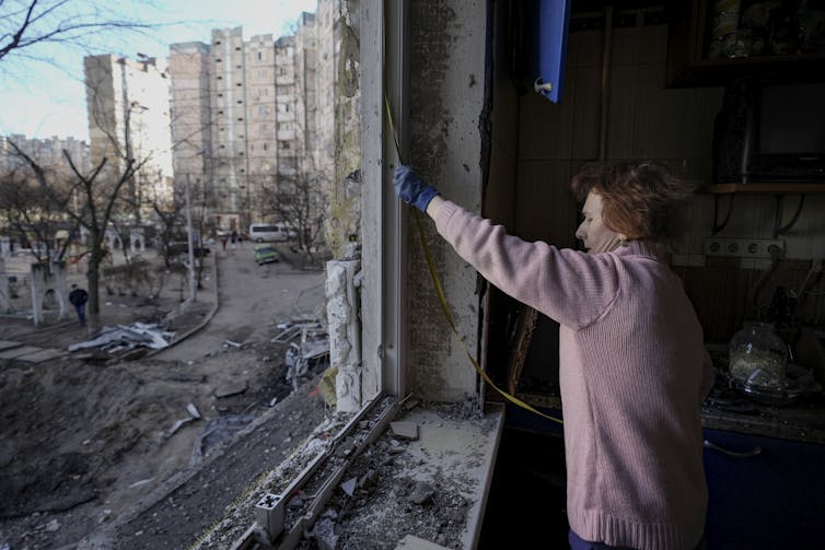 A person wearing a sweater and gloves uses a tape measure on a window