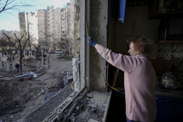 A person wearing a sweater and gloves uses a tape measure on a window