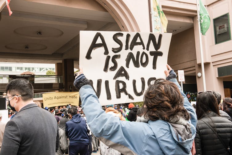 A man holds up a sign that says 'Asian is not a virus.'