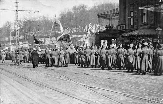 A black and white photo depicts Ukrainian soldiers marching while holding aloft flags.