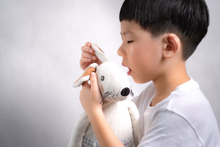a boy whispers into the ear of a stuffed animal
