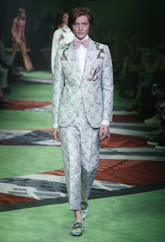 A man in a floral suit walking down a catwalk for Gucci.