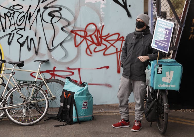 A man leaning against a bike with a cooler that says deliveroo on the back