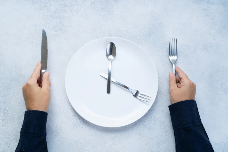 Hands holding silverware next to a dinner plate.