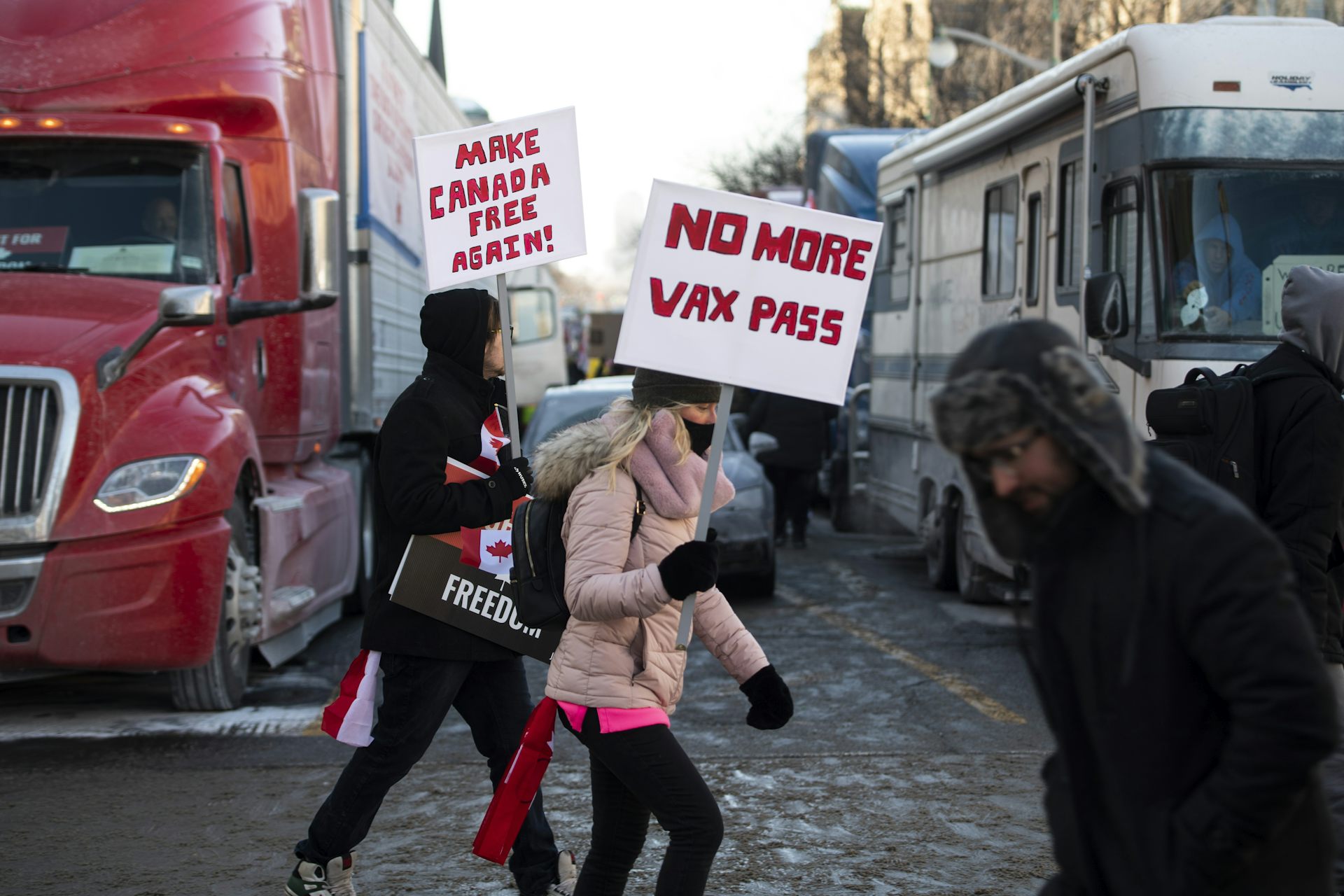 People carrying signs reading 'No more tax pass' and 'Make Canada free again' in front of a parked trucks