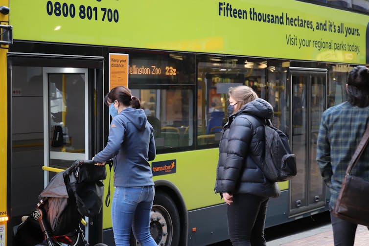 People line up to get on a green bus