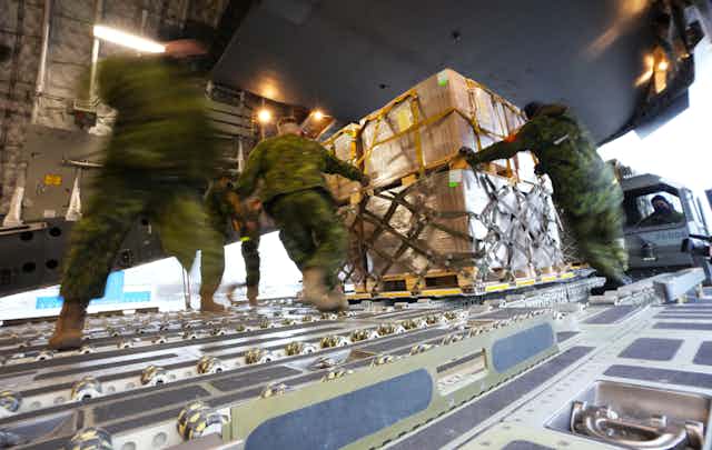 Men in uniforms load cargo onto a plane.