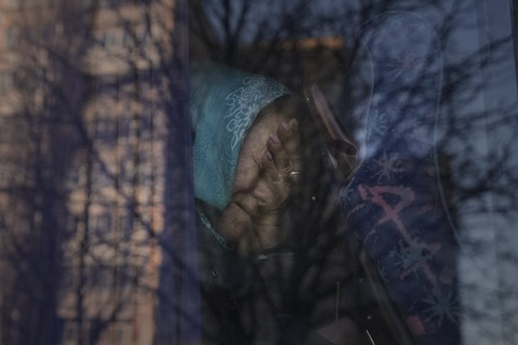 An elderly woman wearing a blue kerchief cries as she sits on a bus.