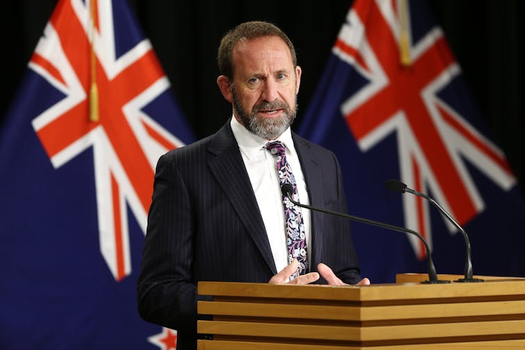 Labour politician Andrew little stands in front of two New Zealand flags.