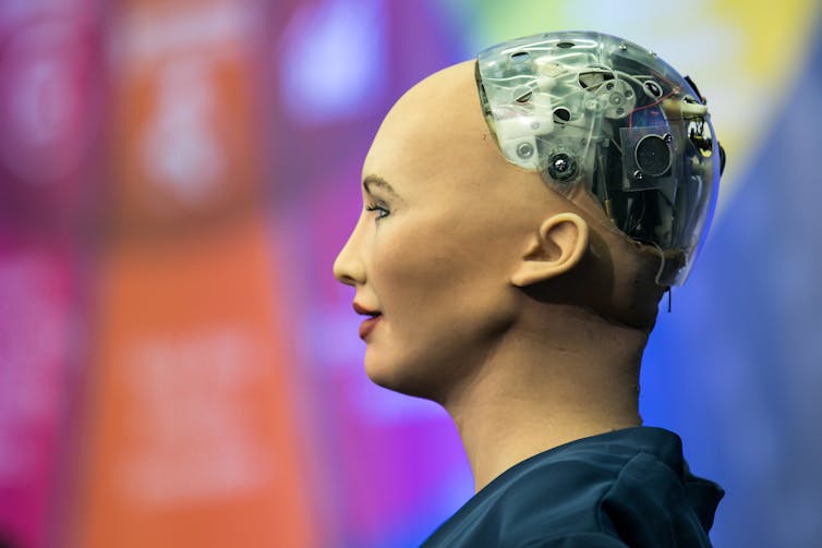 El robot Sophia hablando desde un escenario, detrás de ella, una pantalla donde se puede leer 'AI for GOOD Global Summit'