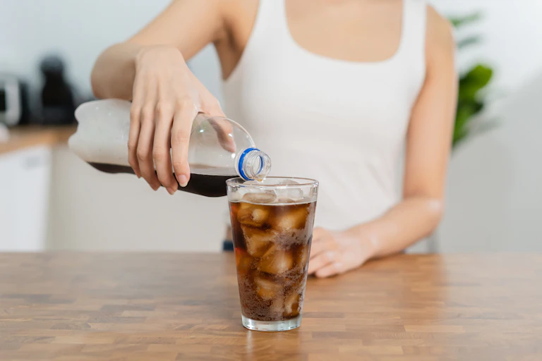 Woman pours diet soda from a bottle into a glass full of ice.