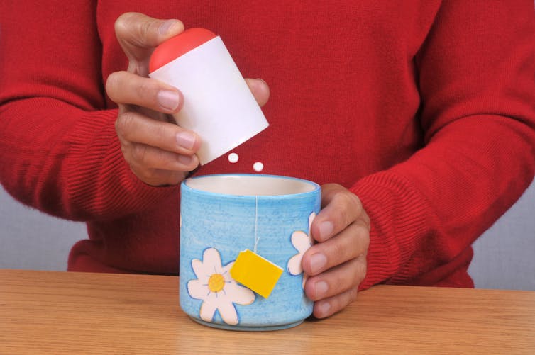 A person puts aspartame sweetener into their mug of tea.