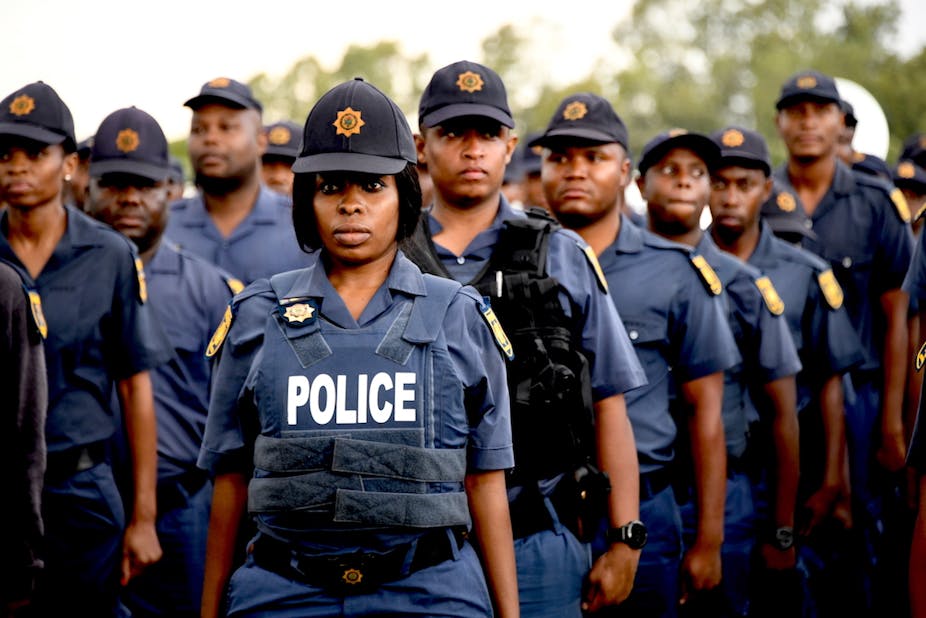  A policewoman wearing a cap and police bulletproof stands to attention along with fellow officers.