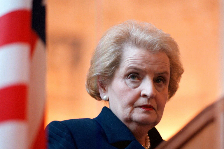 Madeleine Albright stands behind a United States flag.