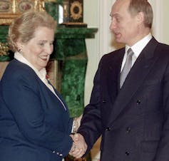 U.S. Secretary of State Madeleine Albright smiles as she shakes hands with Russian acting President Vladimir Putin wearing a suit.