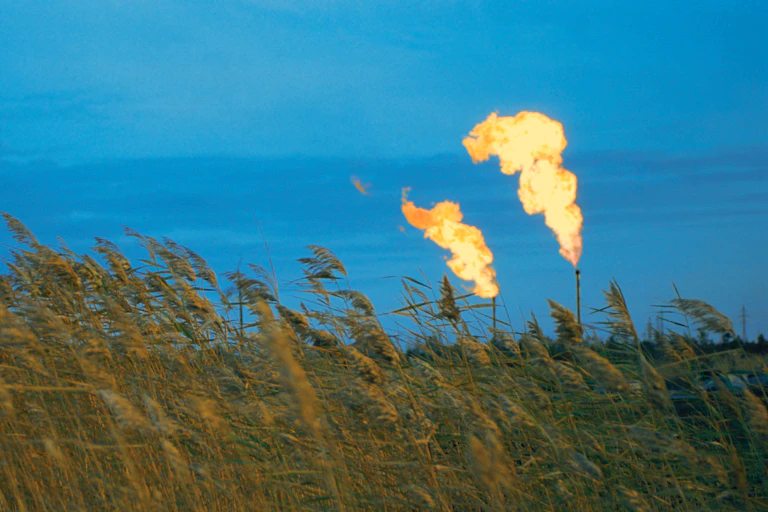 Gas flares against a blue sky with golden wheat in the foreground.