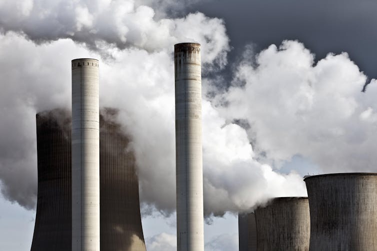 Two chimneys spewing smoke with three cooling towers belching steam behind.