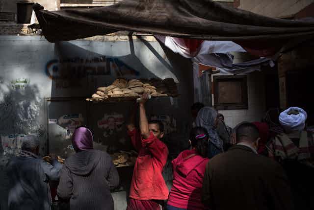 A man holds a tray of round flatbreads overhead and moves through a crowd