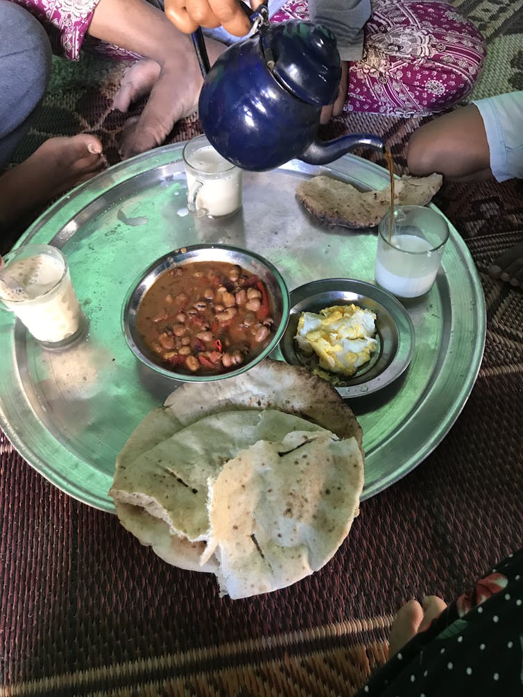 Dishes of egg and stewed beans with flatbread arranged on a tray.