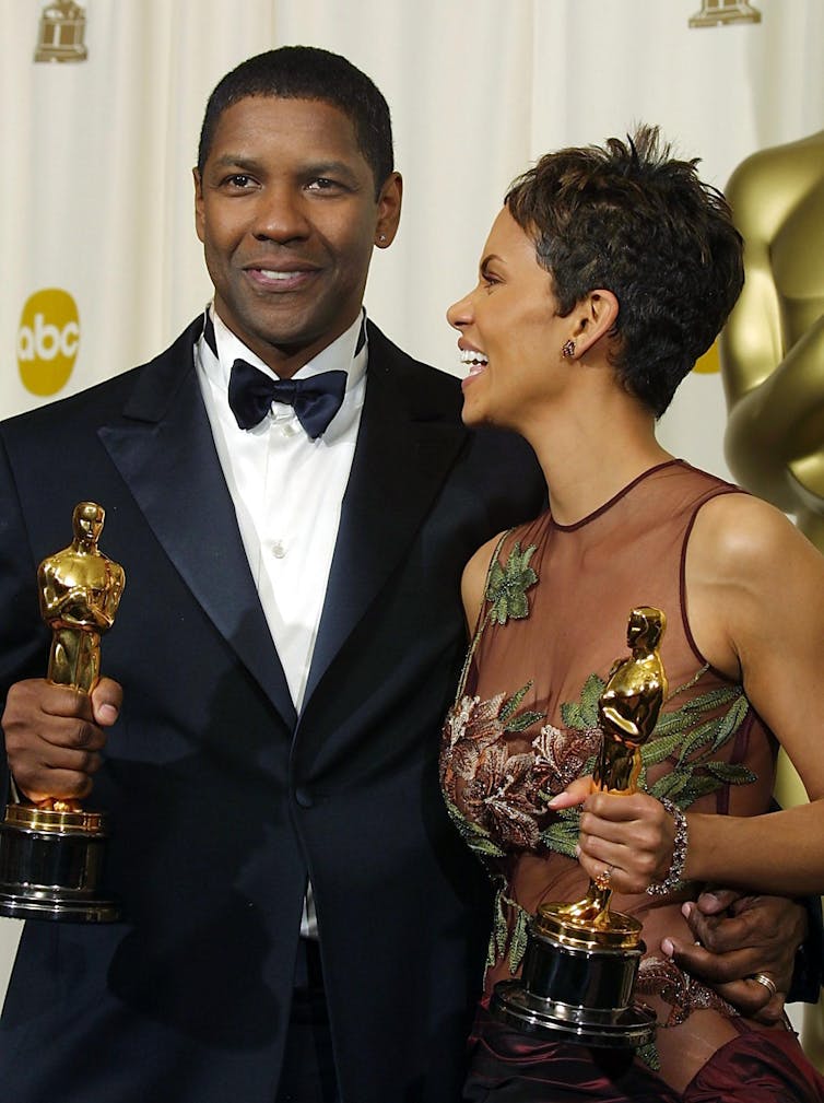 A black man and a black woman hold their gold statues for winning best actor and best actress.