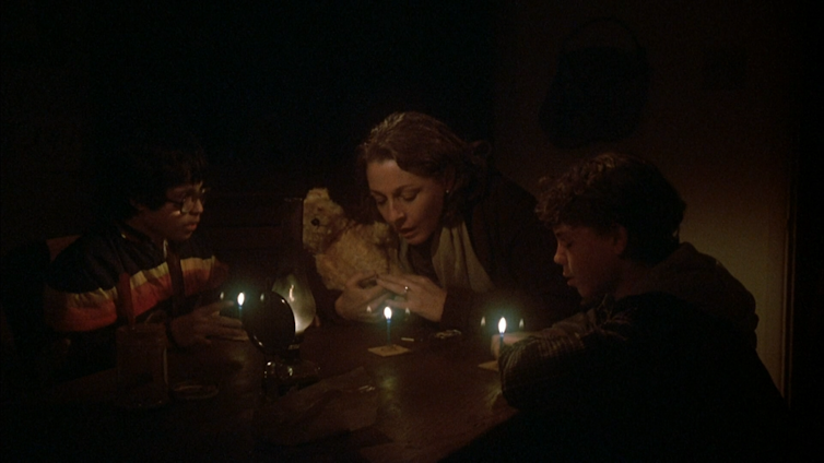 A woman and two boys pray around a candle-lit table.